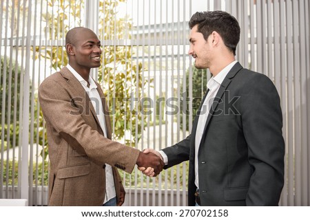 Black businessman shaking hands with a caucasian one wearing suit in a office. Two men smiling