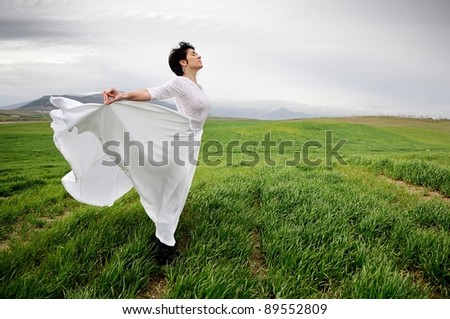 Woman wearing a wedding dress meditating in the meadow against the wind