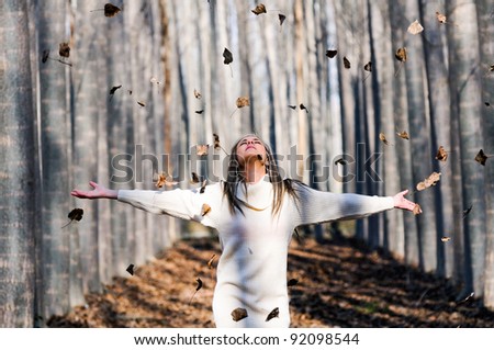 Beautiful blonde girl with open arms and falling leaves in the autumn park