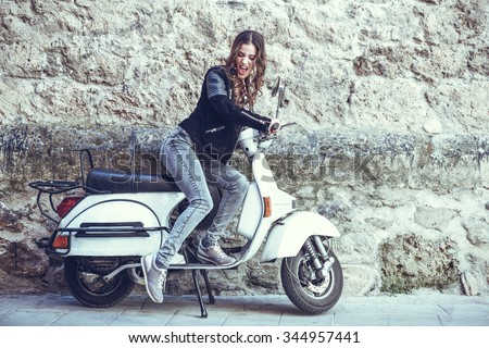Woman launching a old scooter with pedal wearing casual clothes in urban background.