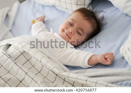 Smiling baby girl lying on a bed sleeping on blue sheets