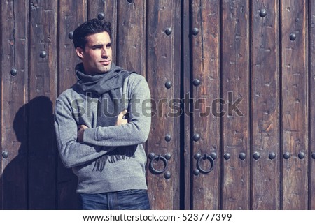 Handsome man wearing winter clothes in wooden background. Young male with sweater and scarf.