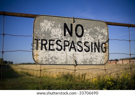 No trespassing sign against backdrop of farmland being encroached by housing development. Urban sprawl concept.