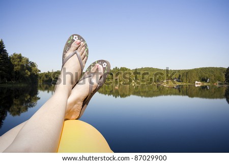 Legs resting on a paddle boat in calm lake water shot in muskoka cottage country ontario