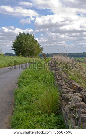 Country road in Cotswolds England background with blue sky and clouds
