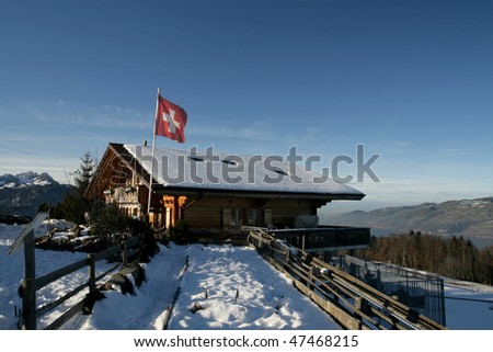 Snow covered wooden cabin with Swiss flag in the sunset