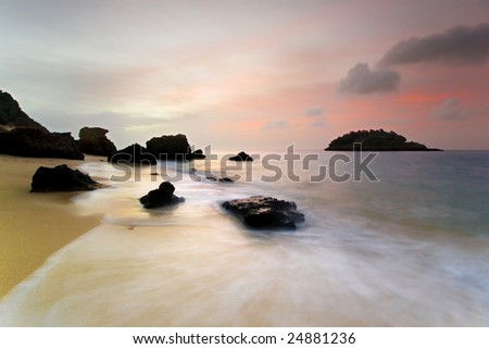 Beach scene at sunrise, with pink sky, rocks, island and moving water