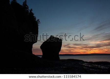 As the sun rises in the background, you can make out the silhouette of one of the famous Hopewell Rocks flowerpot formations.Taken at low tide in New Brunswick, Canada.