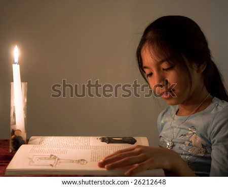 Young school girl reading a book by candle light.