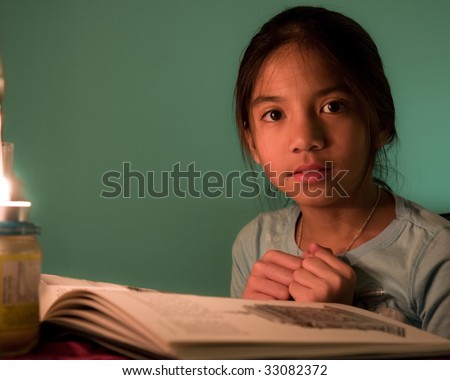 Young school girl takes a pause from reading a book. Her face partially lit by candle light.