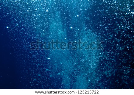 The picture shows underwater bubbles which raise from the depth of blue sea