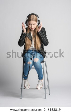 Adorable smiling girl in wired headphones is sitting and listening music from her own smartphone