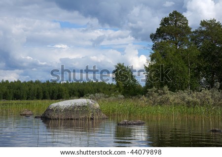 The beautiful picture of Karelian forest at the edge of a lake, and some huge boulder in this lake