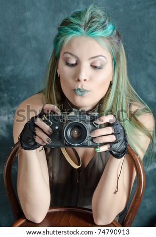 Photo session of the pretty young blonde girl with green hair in the steampunk style with photo camera