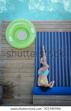 woman laying on a soft mat which attach to a wooden balcony of a water villa bungalow at Maldives, she has her face partially covered by black hat and there is a light green life buoy next to her