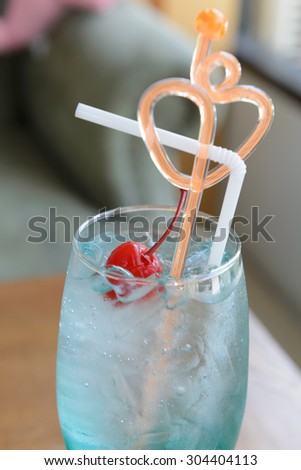 close up and soft focus of blue ocean, curaÃ§ao with red maraschino cherry on top, heart shape stirring, focused on the red cherry and shot at ambient light in a cafe