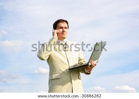 businessman calling by the phone and holding laptop over blue sky with clouds