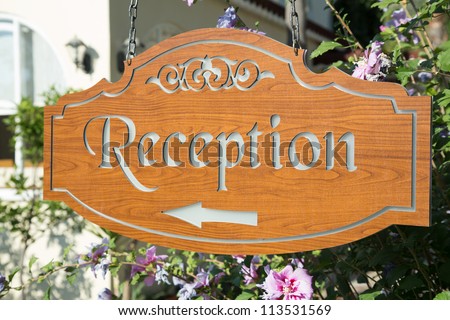 Wooden outdoor  hotel reception pointer located among blossoming flower bushes on a deep blue sky background