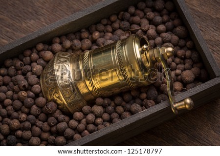 Metal pepper mill in eastern style lying in a wooden box filled with sweet-scented pepper