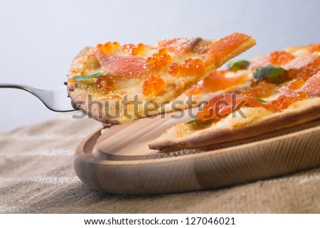 Slice of pizza with salmon and salmon caviar taken from wooden pizza peel with steel pizza slice server