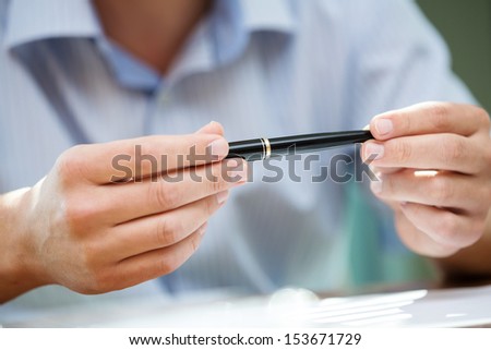 Man\'s hands holding a black pen in both arms in a thinking gesture during a meeting or negotiation