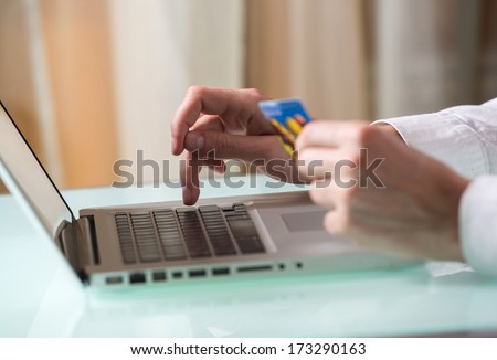 Man\'s hand entering data using laptop while holding a credit card in the other hand
