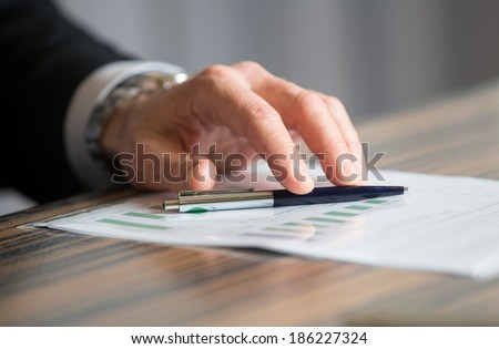 Man\'s hand holding a black pen over a diagram on a meeting dedicated to financial analysis