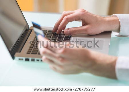 Man\'s hand entering data using laptop while holding a credit card in the other hand