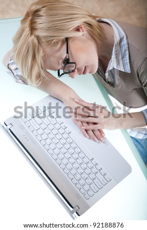 Tired woman in glasses lying on the table next to laptop