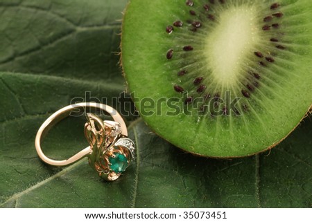 golden ring with emerald on green grass and kiwi