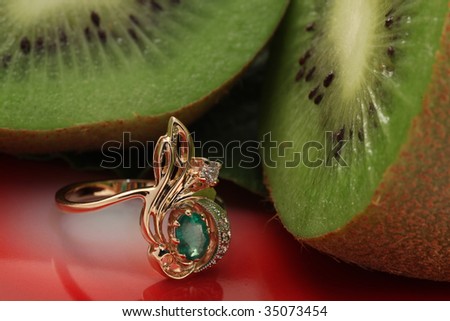 golden ring with emerald on green grass and kiwi
