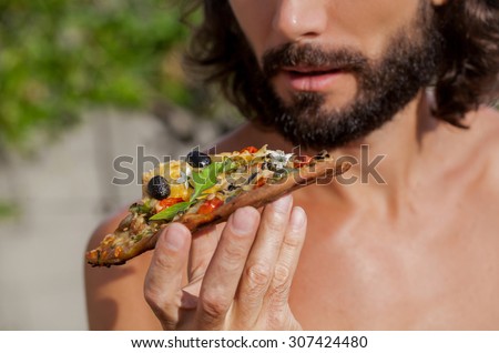 hungry man biting, eating slice of pizza  portrait of a young man eating pizza against a nature background portrait of a young beautiful man eating a slice of pizza