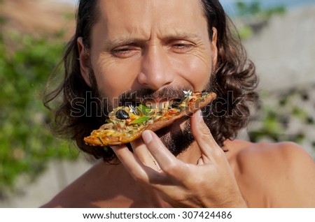 hungry man biting, eating slice of pizza  portrait of a young man eating pizza against a nature background portrait of a young beautiful man eating a slice of pizza