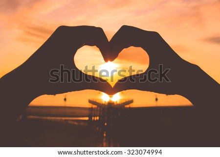 Silhouette hand in heart shape on sunrise over the sea,Vintage style photo with custom white balance, color filters
