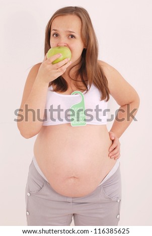 Pregnant woman eating an apple. On a woman hangs a sign Do Not Disturb Baby Nursing on grey background