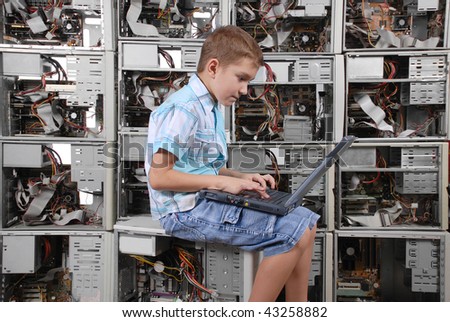 The boy works behind a portable computer on a background of a wall from old computers. Horizontal orientation.