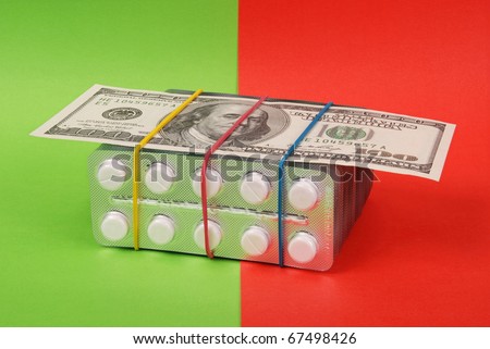Hundred dollars lays on packing of white tablets. Red and green background.