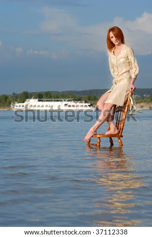 Portrait of beautiful woman on chair in river water with ship on background