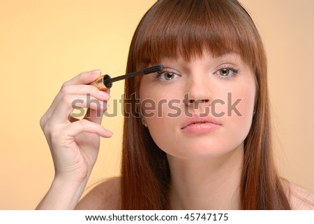 Young beautiful woman making up eyelashes on yellow