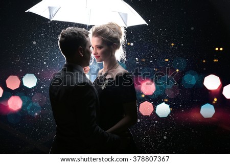 Beautiful couple man with woman  with  white umbrella in flash lights and rain drops