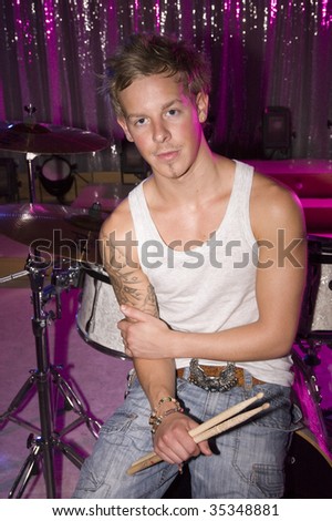 Young adult male drummer wearing vest sitting in front of drum kit