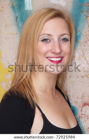 Head and shoulders photo of pretty teenage girl in black top with pink lipstick, posed in front of graffiti door.