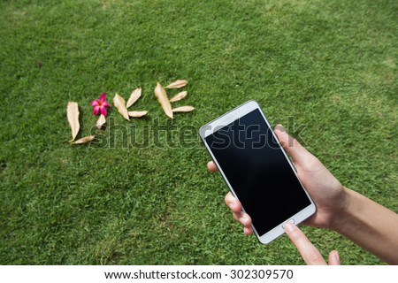 woman hand hold and touch screen smart phone, cellphone over blurred lawn or lawn background