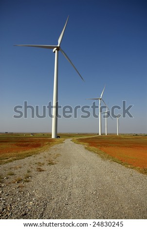 A service road winds between the wind turbines in a rural area.