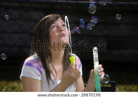 A teen girl blows bubbles with a bubble wand.