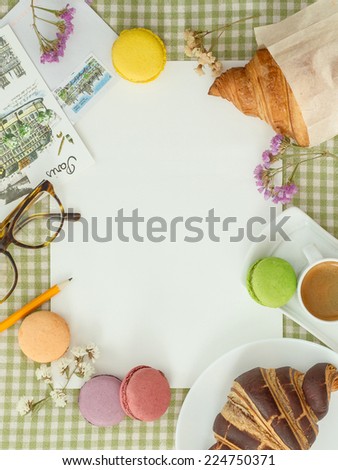 Blank sheet of paper for notes on a checkered tablecloth with coffee, macaroon, croissants and postcards in the French style