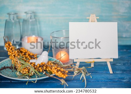 Buckthorn branches with white bird figurine on a blue plate and mini easel with blank canvas
