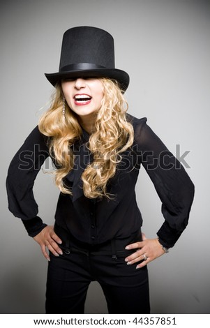 Laughing young pretty girl in black with top hat in studio