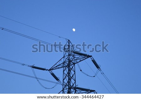 Electricity pylon against twilight sky with moon in background.