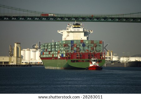 A container and tug boat move under a bridge as they arrive in port.